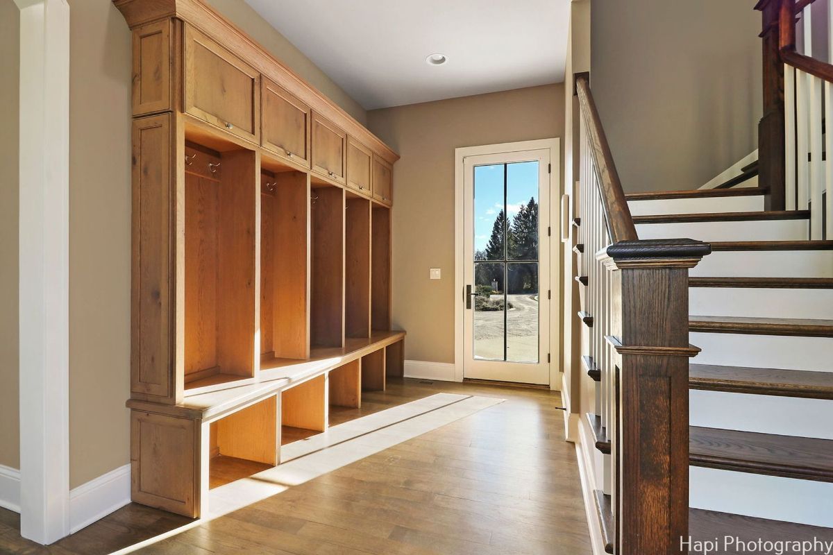 Hallway with a built-in wooden bench and cubbies, a glass door leading to the outdoors, and a staircase with a dark wood railing.