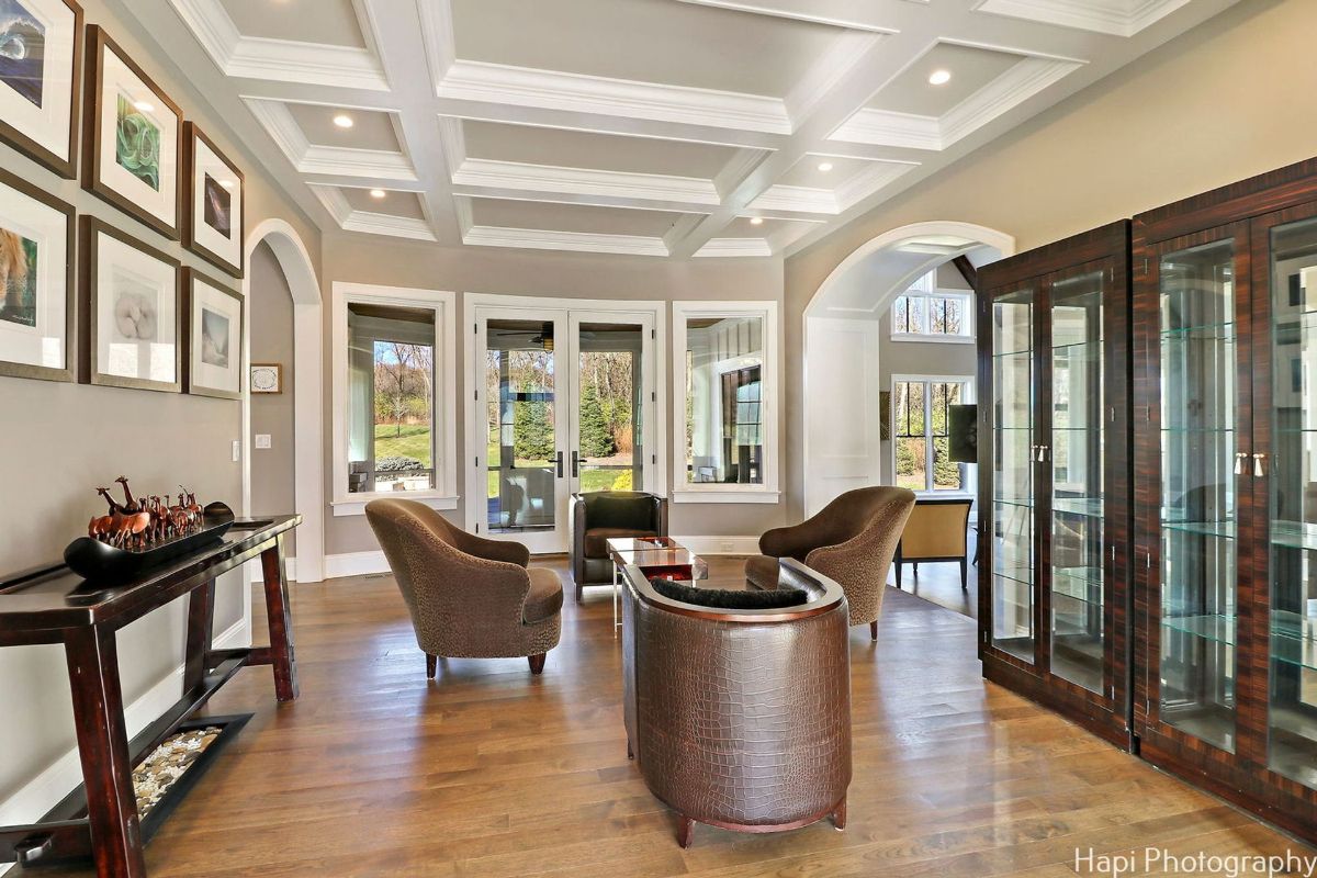 Living room with hardwood floors, a coffered ceiling, and large windows overlooking a garden.