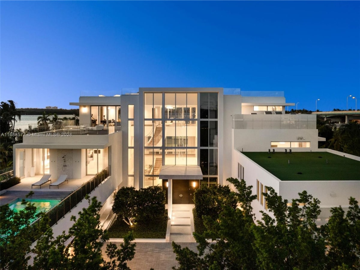 Mansion is predominantly white with large windows, and it is illuminated.