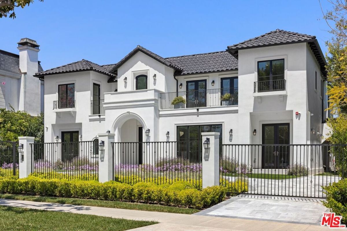 Impressive Spanish-style home features a dark roof, white walls, and a black metal fence.