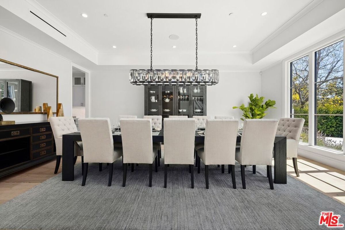 The formal dining area is highlighted by a large rectangular table surrounded by numerous chairs, all under a dramatic chandelier.