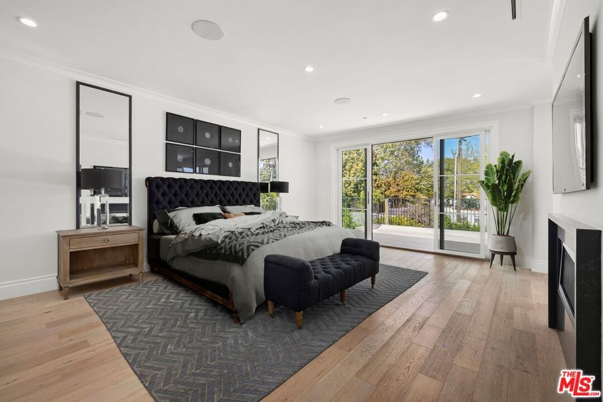 Master bedroom with a large bed, nightstands, and sliding glass doors leading to an outdoor area. The floor is light-colored wood.