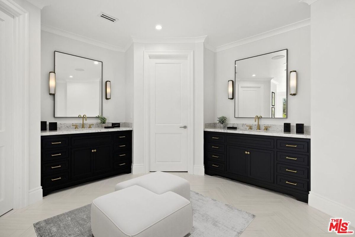 Bathroom with double vanities, large mirrors, and light-colored floors and walls. The vanities are dark-colored wood.