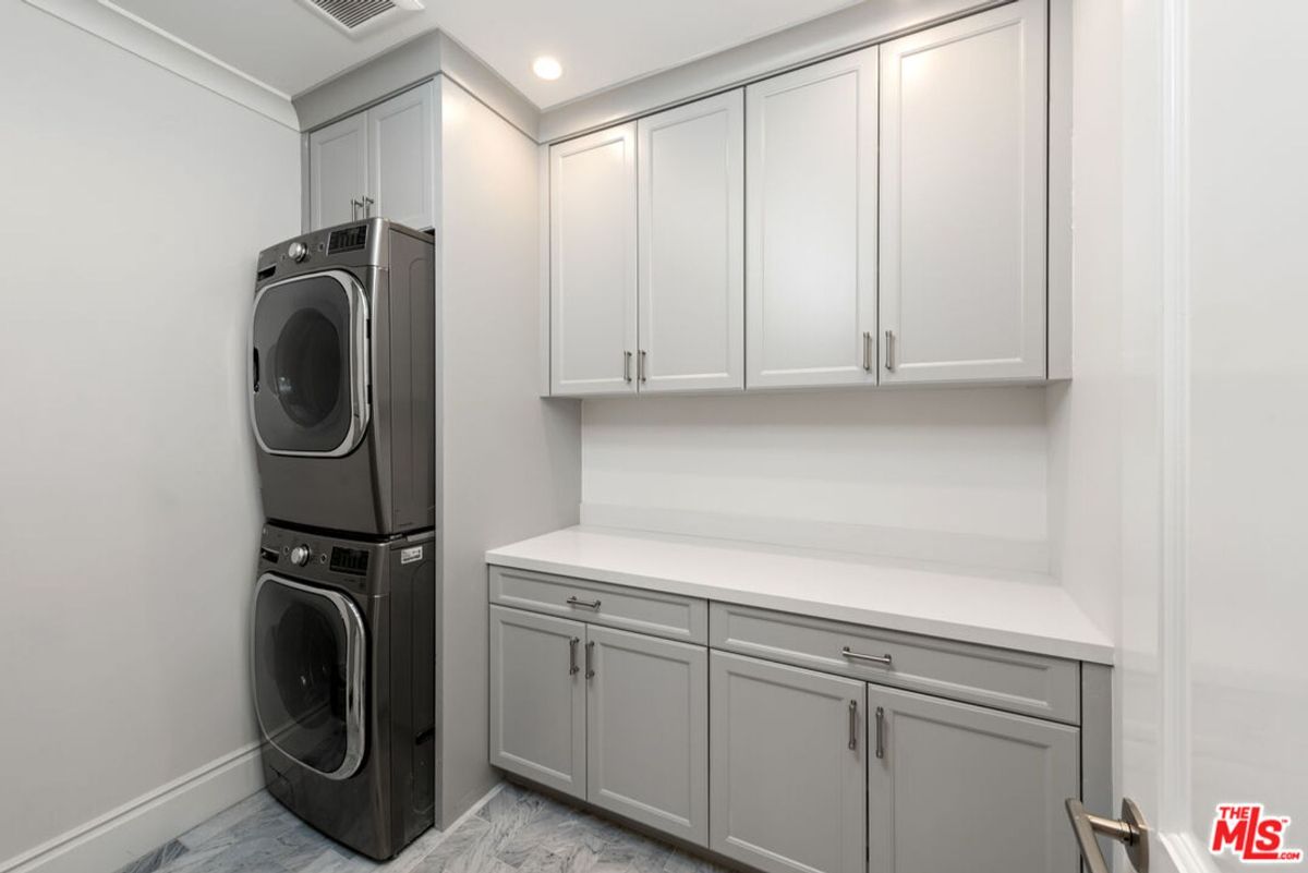 Laundry room with a stackable washer and dryer, and light gray cabinets. The countertop is white.