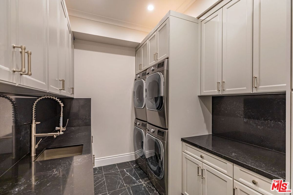 Laundry room with dark countertops, light-colored cabinets, and a stackable washer and dryer. There is also a sink.