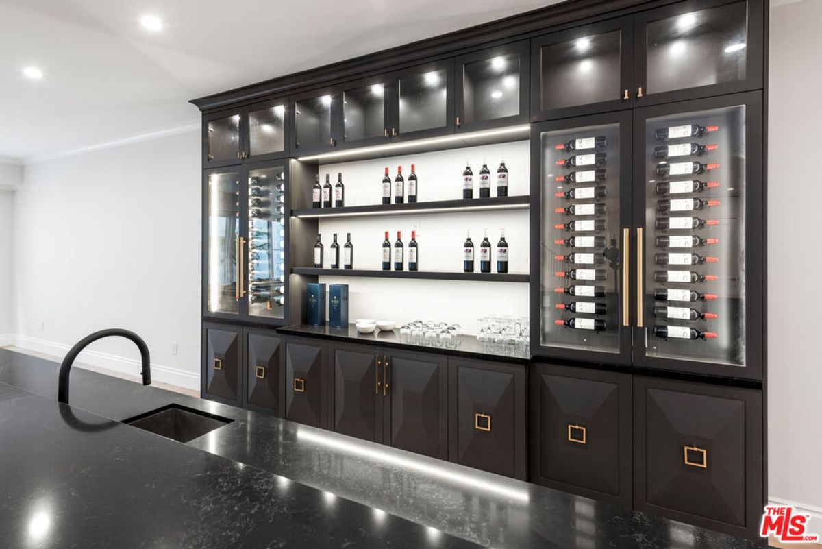 Wine cellar with dark-colored cabinets, glass-fronted wine refrigerators, and shelves for wine bottles. There is also a sink visible.