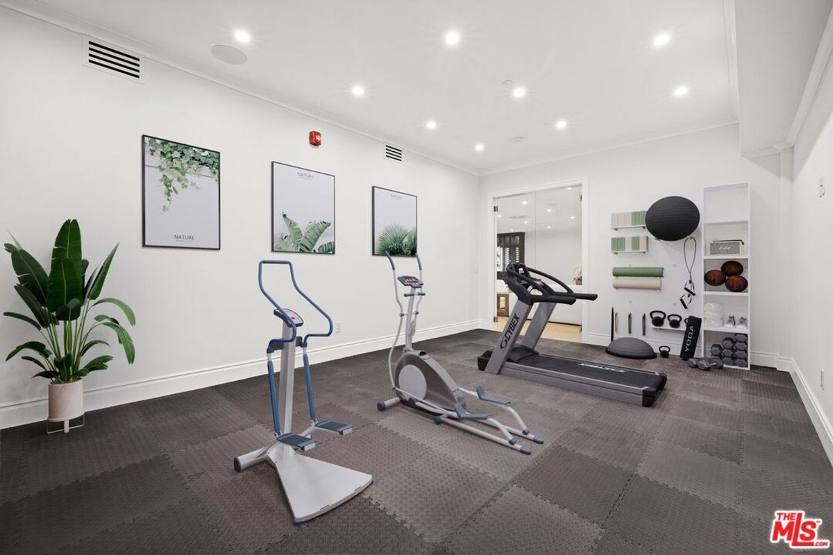 Home gym with a treadmill, elliptical machine, and other exercise equipment. The walls are white, and the floor is covered in gray mats. 