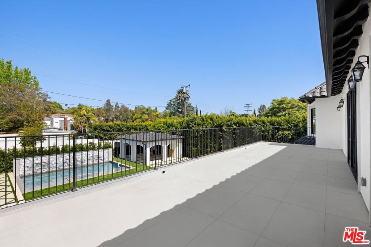 View from a rooftop deck overlooking a swimming pool and surrounding landscape. The deck is light-colored tile, and there is a black metal railing.