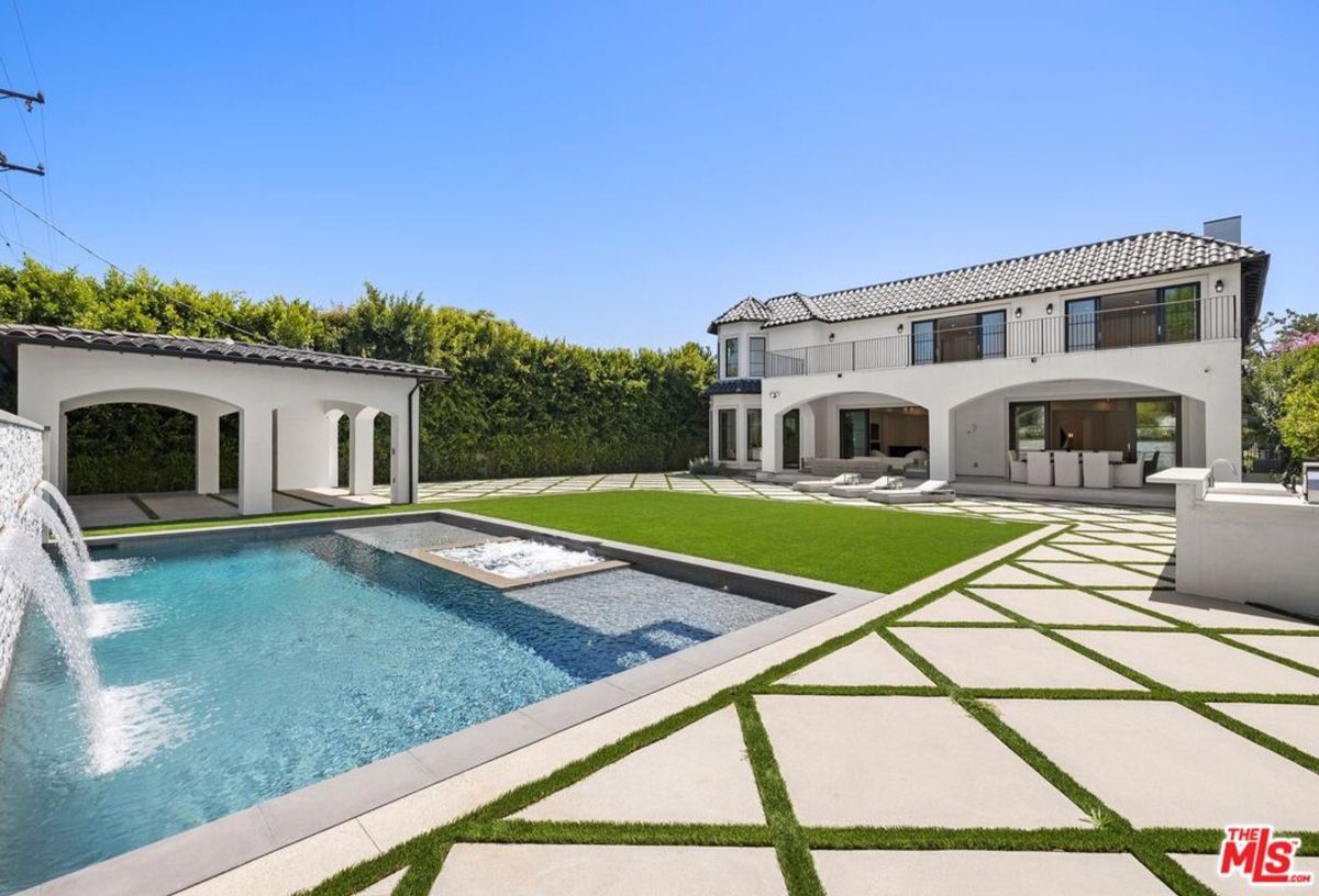 Backyard with a swimming pool, spa, and a large house. The landscaping includes a grassy area and a paved patio. There is also a water feature visible.