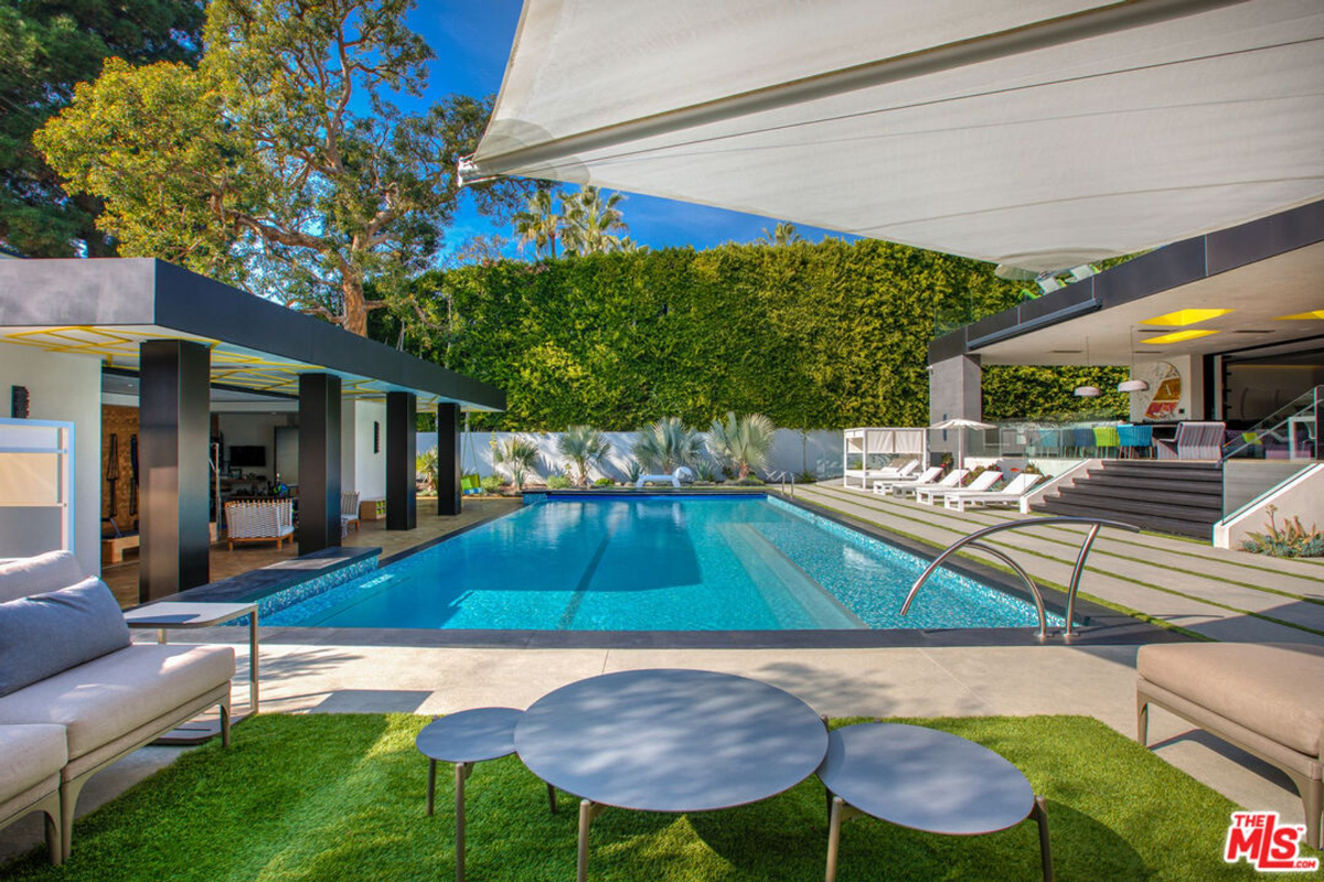 Luxury swimming pool with a modern architectural setting. There's a covered patio area and lounge chairs surrounding the pool.