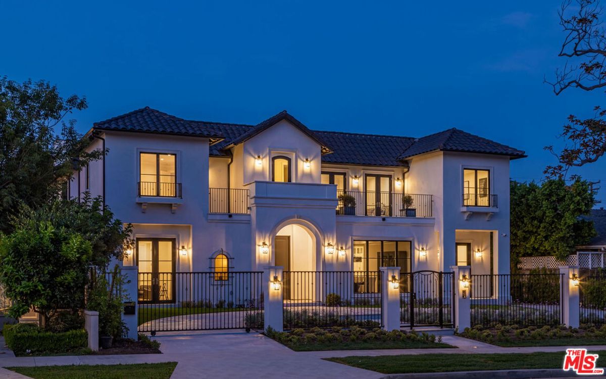 Night illuminates a grand, two-story house, its many windows glowing warmly.