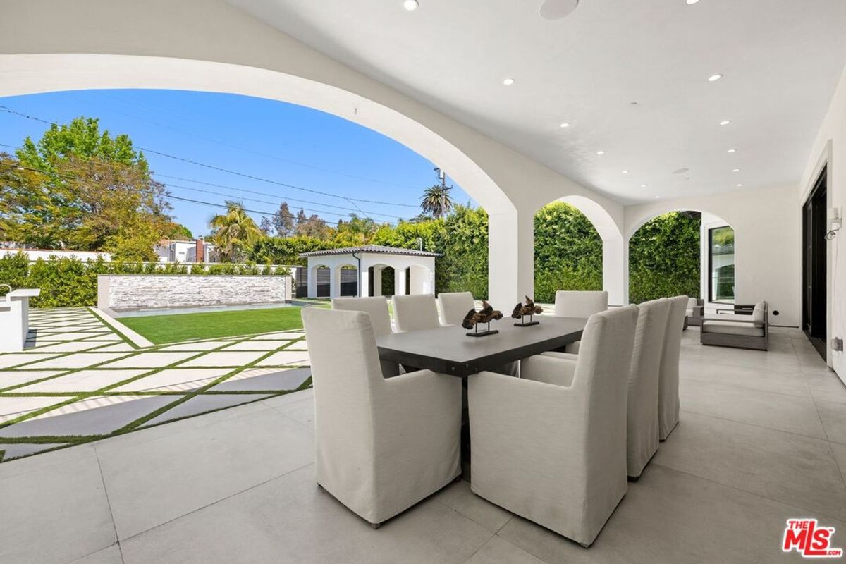 Outdoor patio furniture sits under an arched covered area overlooking a spacious backyard.