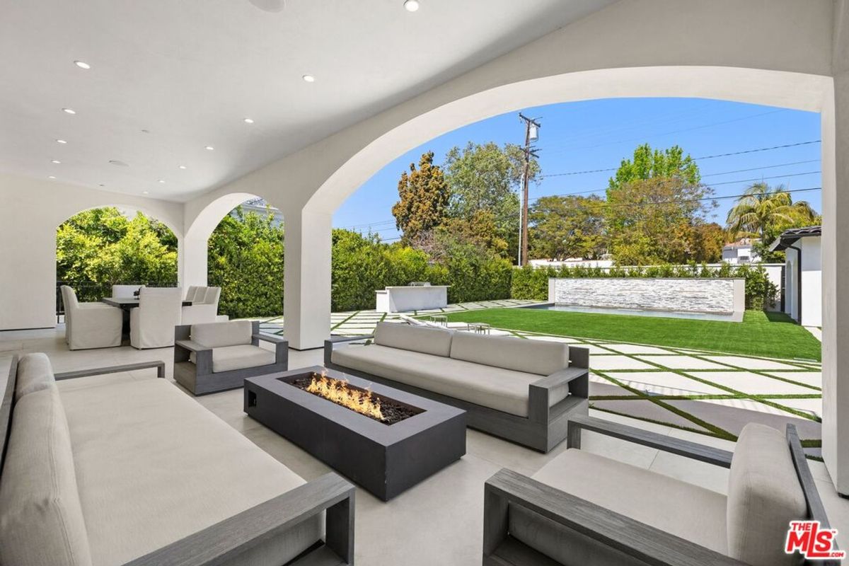 Modern outdoor furniture arrangement centers around a fire pit, all under a covered patio overlooking a neatly landscaped lawn.