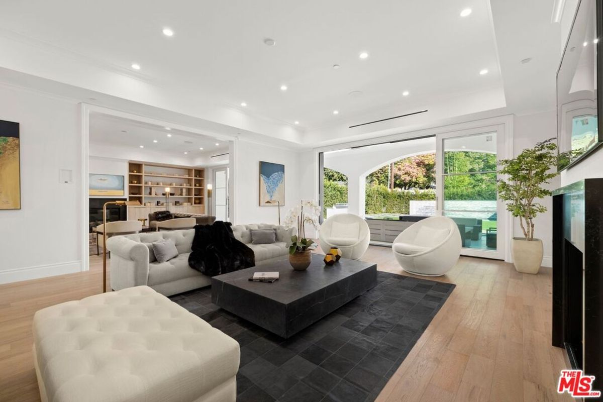 Bright, open living area features a large sectional sofa, two modern accent chairs, and a spacious coffee table, all centered around a view of the outdoors.