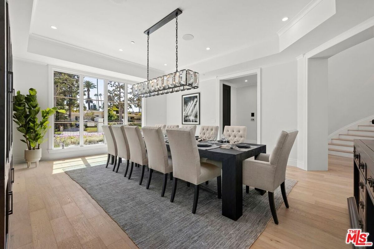 Formal dining room features a large table with many chairs, a statement chandelier, and large windows.