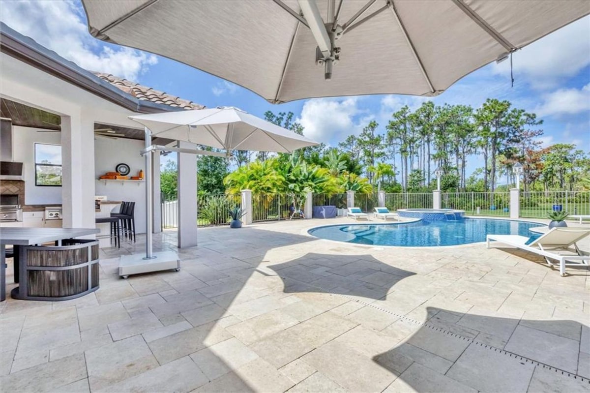  Luxurious outdoor pool area. A kidney-shaped pool is surrounded by a large patio with light-colored stone pavers.