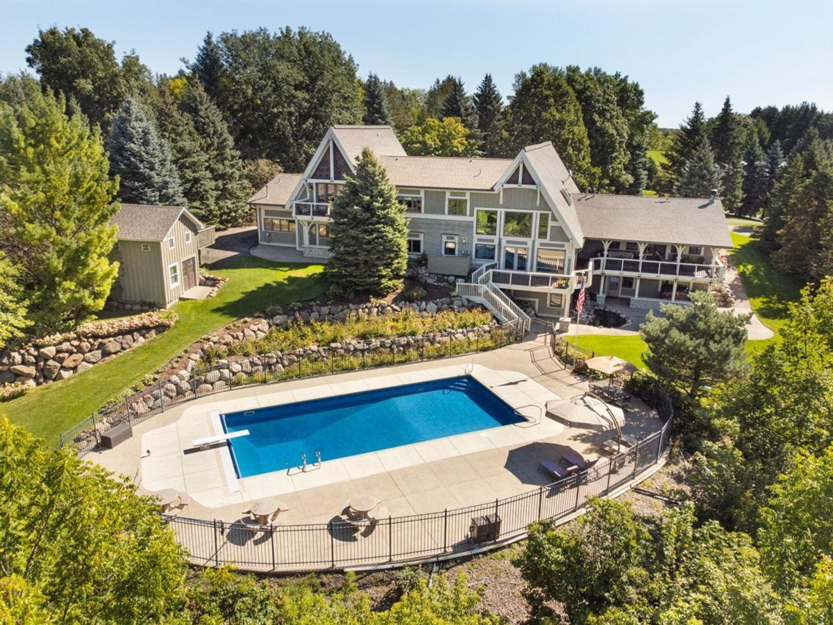 An expansive home with a large swimming pool is situated on a wooded lot.