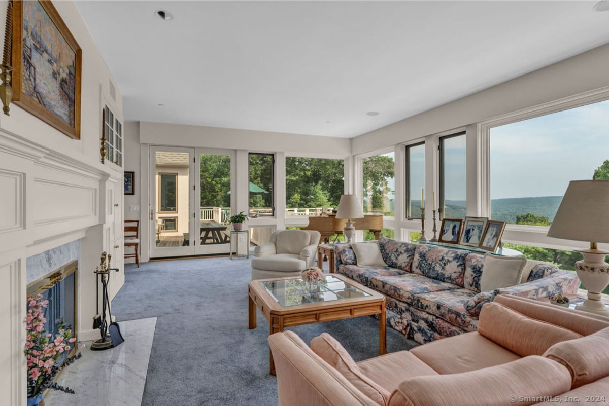 Large windows showcase a scenic view in this bright living room. Light-colored furniture and a fireplace create a comfortable and inviting atmosphere.