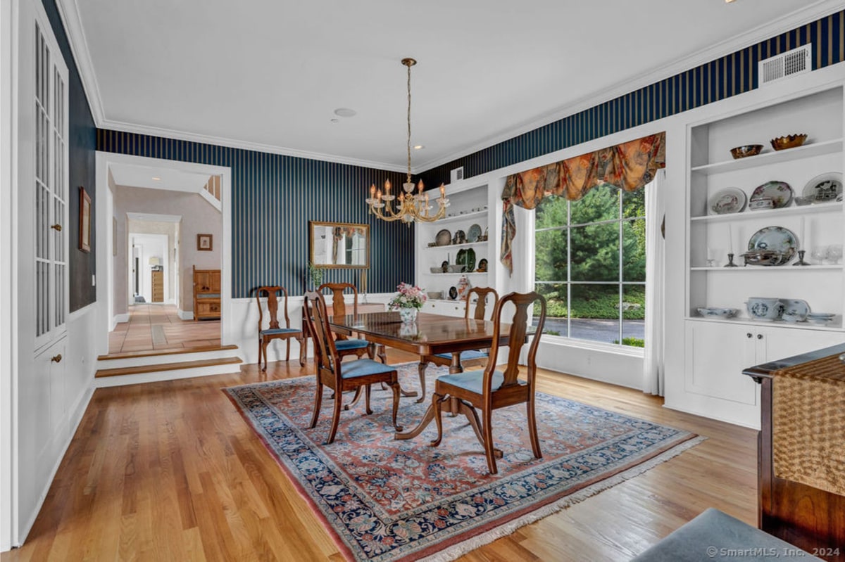 Formal dining room features dark blue paneled walls and hardwood floors. A large ornate chandelier hangs above a wood dining table surrounded by chairs, and built-in shelving units.