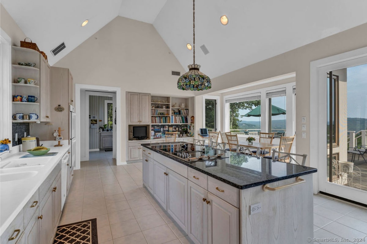 Kitchen island with a dark granite countertop and a built-in cooktop. Floor-to-ceiling windows provide stunning water views.