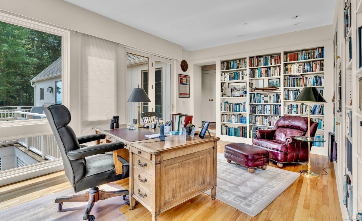 Home office with a large desk, a comfortable leather armchair and ottoman, and expansive built-in bookshelves. Large windows provide a view of the outdoors, creating a bright and inviting workspace.