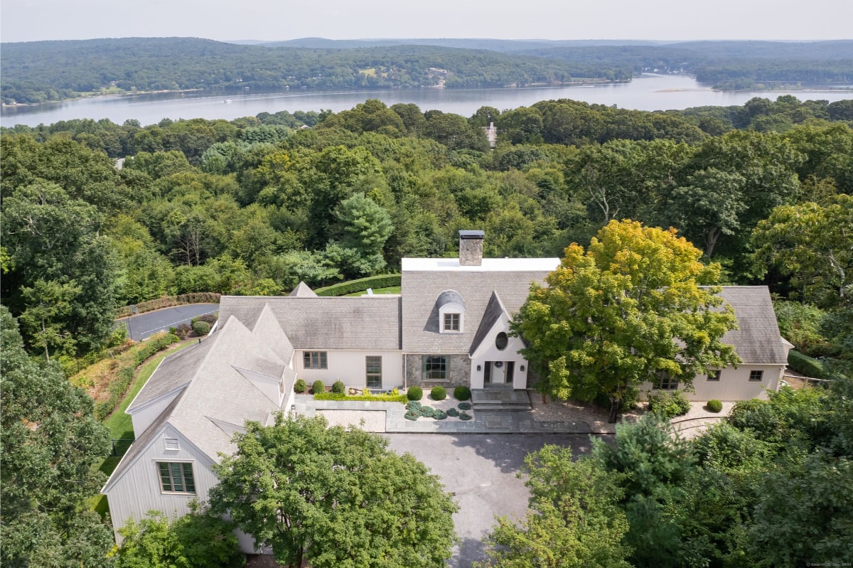 Aerial view of mansion nestled in a wooded area overlooking a lake or river.