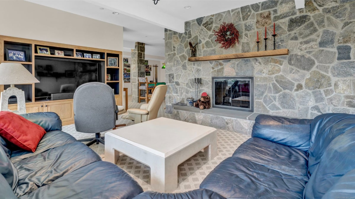 Family room with a large stone fireplace as a focal point. A sectional sofa and built-in entertainment center complete the comfortable, somewhat dated, space.