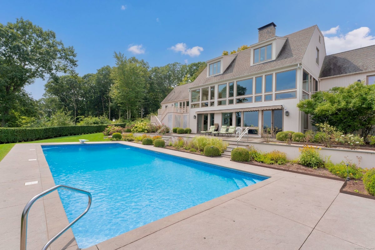 The mansion has many windows that overlook the pool, which is rectangular and well-maintained.