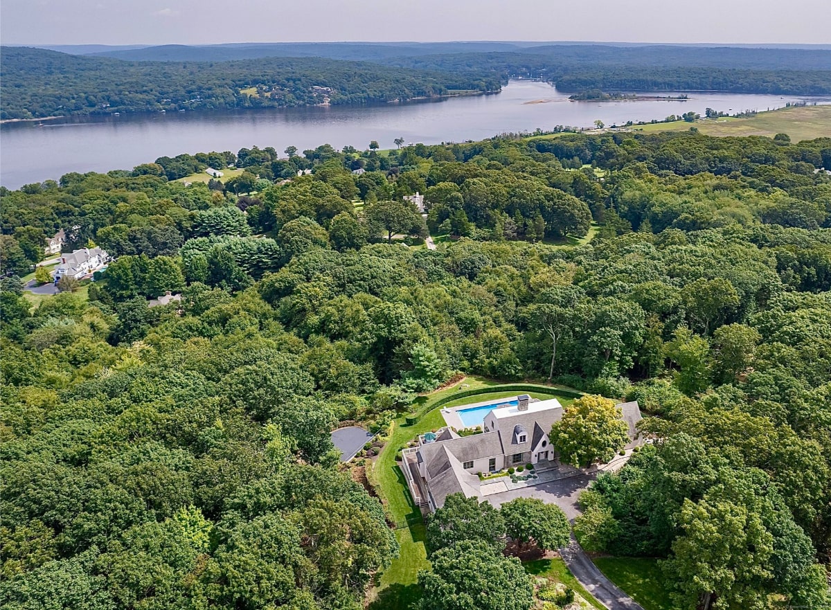 Aerial photograph of a large house situated on a wooded lot overlooking a body of water.