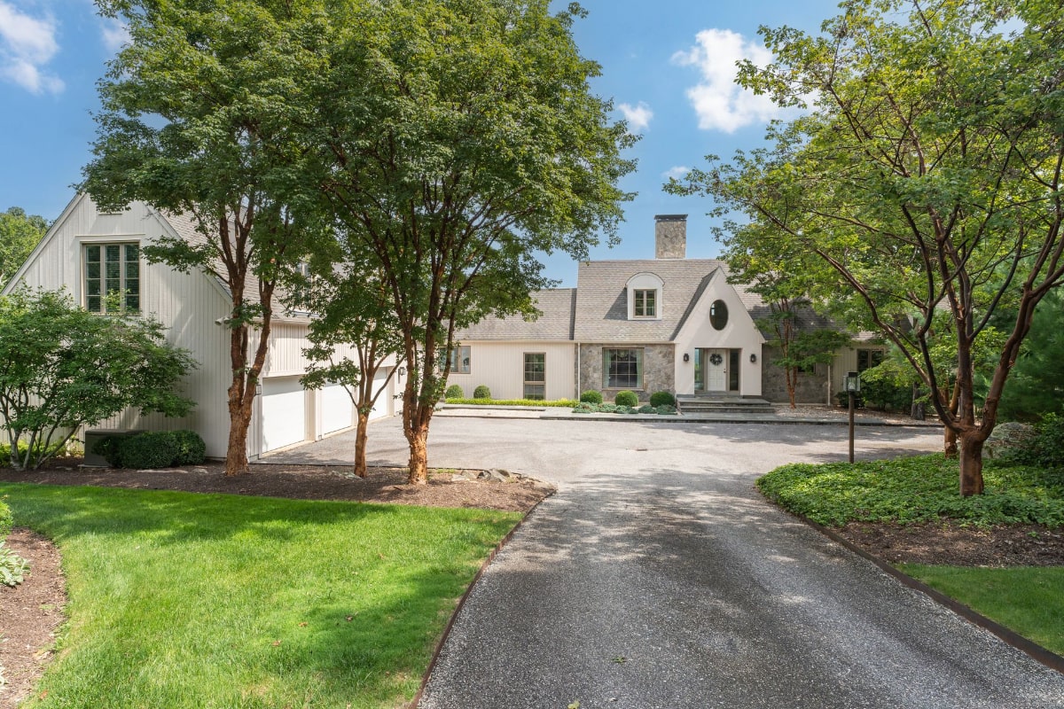 Light-colored house with a stone facade and a long driveway.