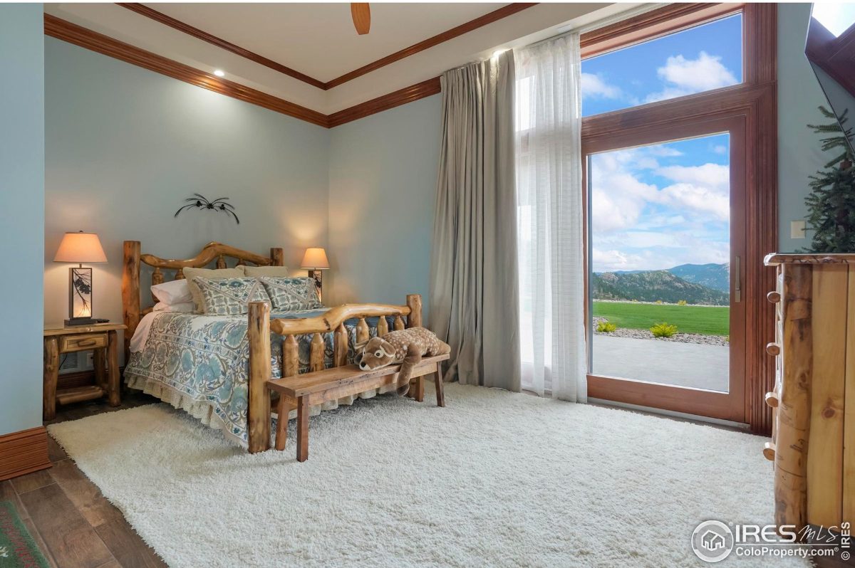 Rustic bedroom features a log bed frame, soft blue walls, and a view of the outdoors.