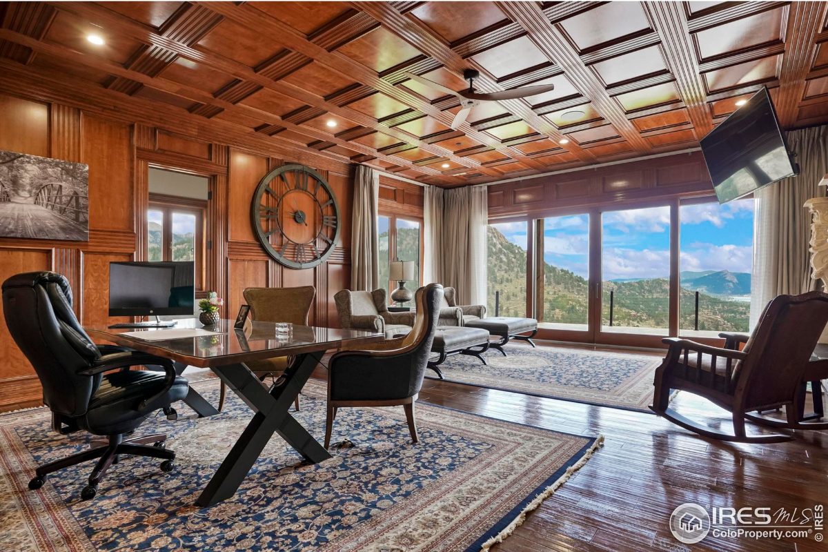 Wood-paneled study features a large clock, expansive windows with mountain views, and a comfortable seating area.