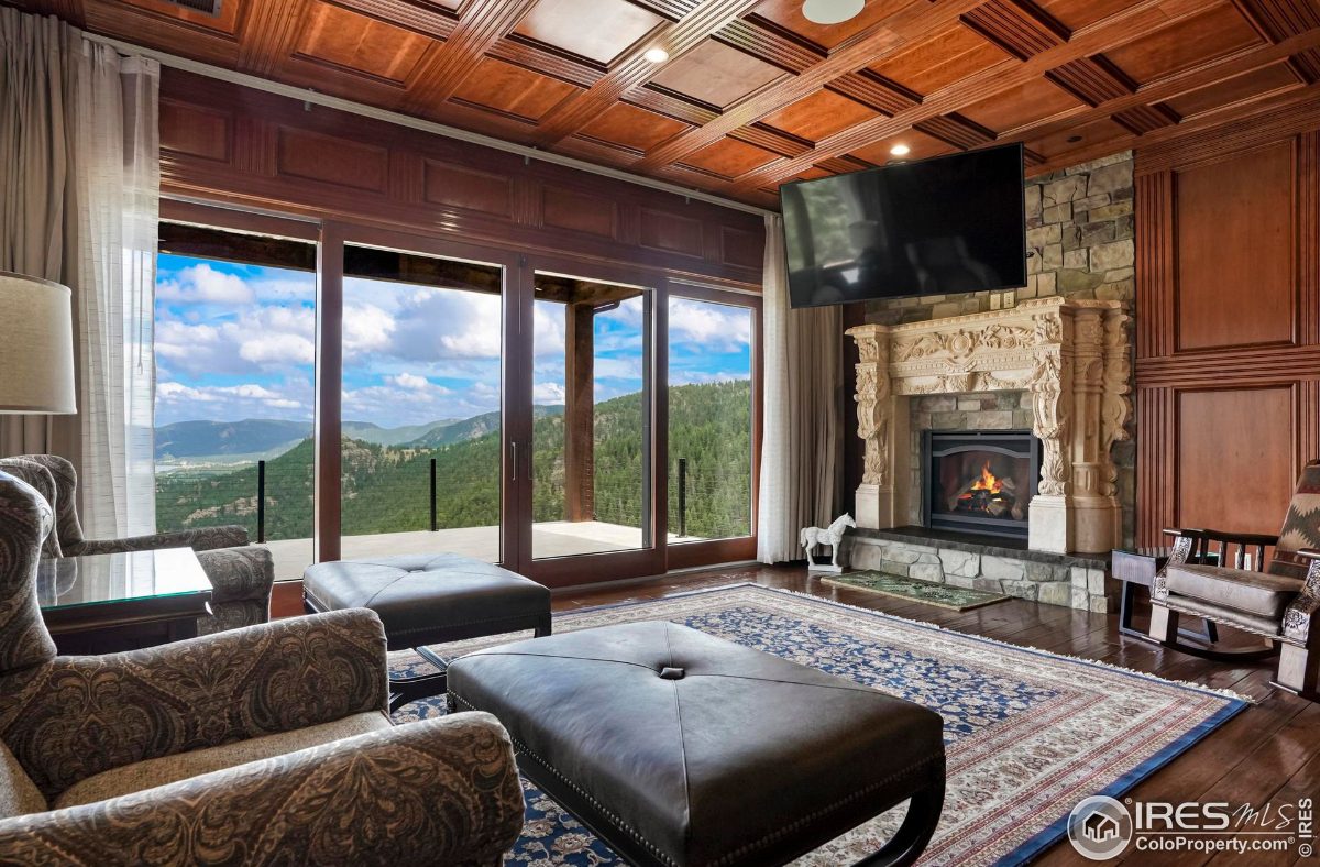 Relaxing living area features a stone fireplace, large windows showcasing mountain vistas, and comfortable seating.