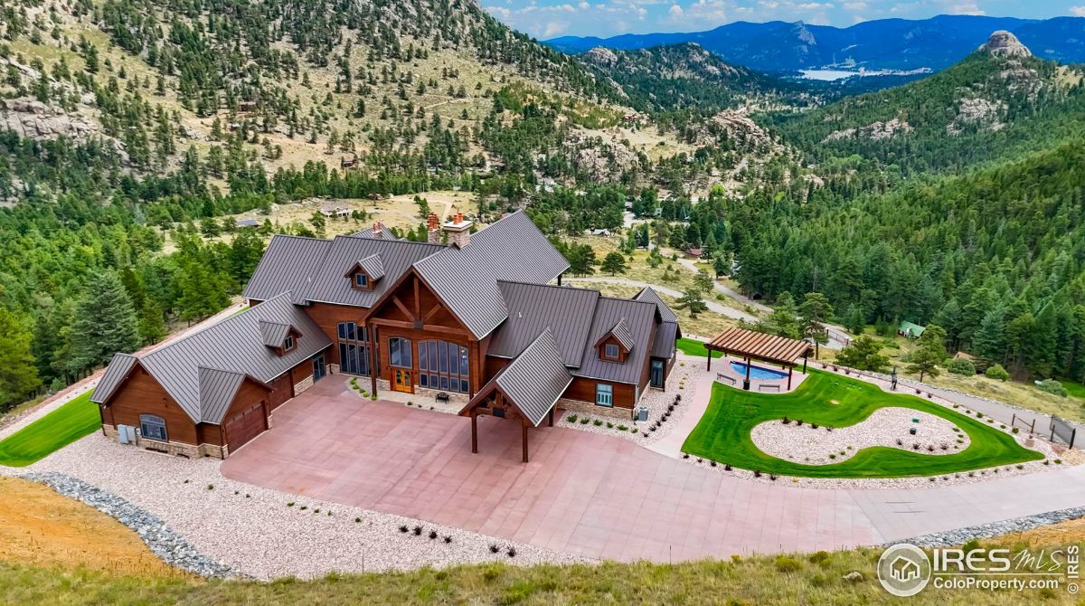 An aerial view reveals a large, rustic-style home nestled in a mountainous region, complete with a sizable courtyard and outdoor amenities.