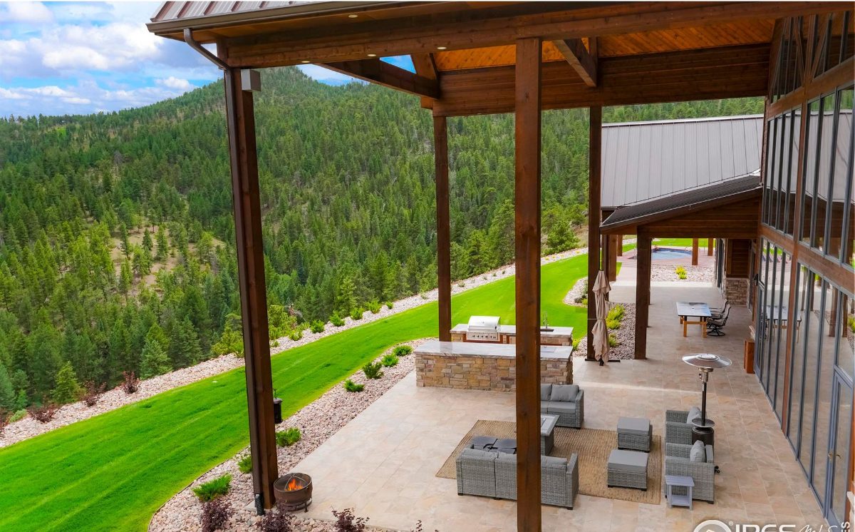 Outdoor patio area features a stone grill, seating area, and stunning mountain views.