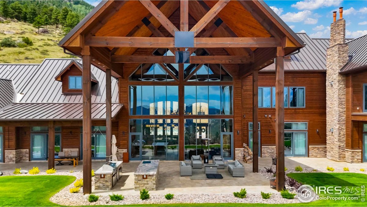 Modern mountain home boasts a large covered patio with an outdoor kitchen and expansive glass doors.