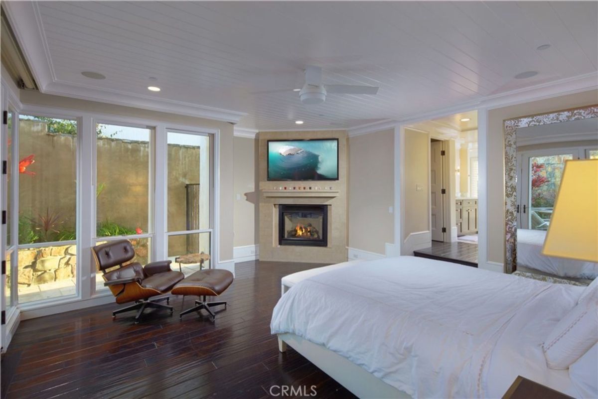 A bedroom with a fireplace and large windows offers a view of a courtyard.