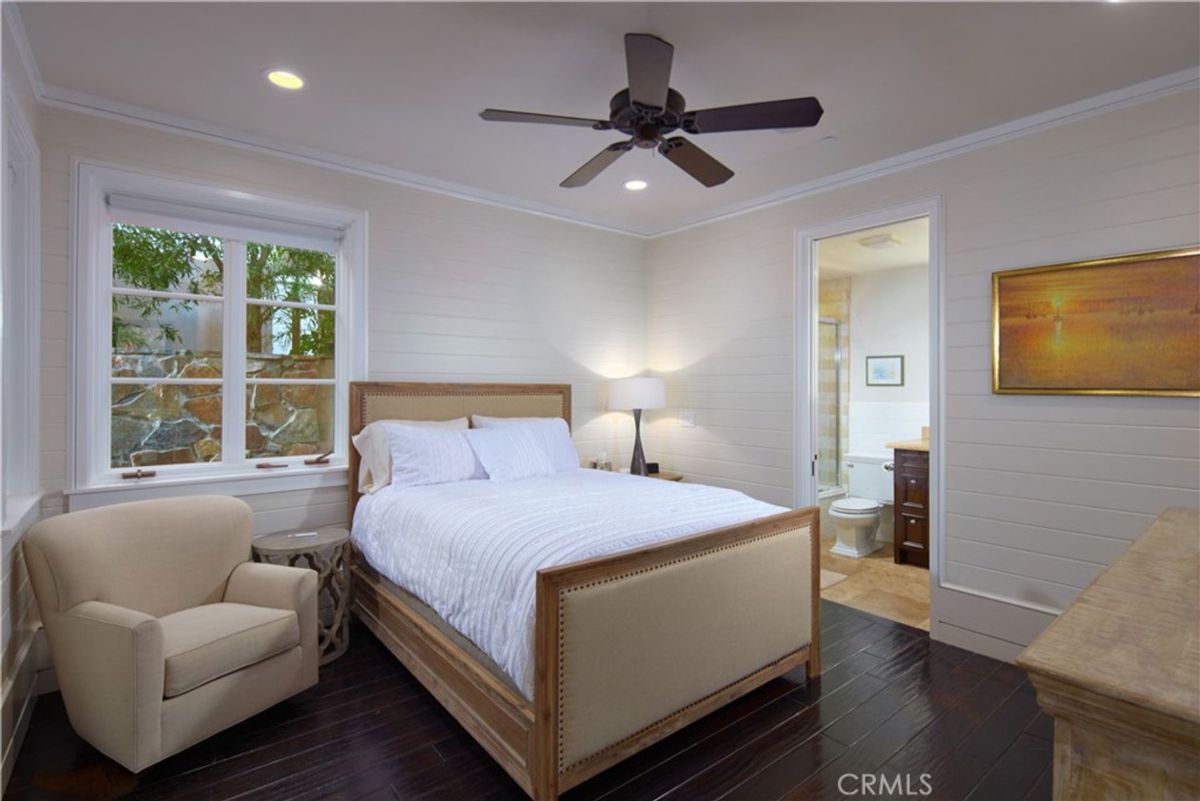 Bedroom with dark hardwood floors and a view of a stone wall from the window.