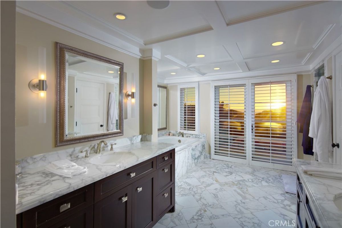 Bathroom with a large mirror and double sinks. The floor and walls are marble. French doors open to a view.