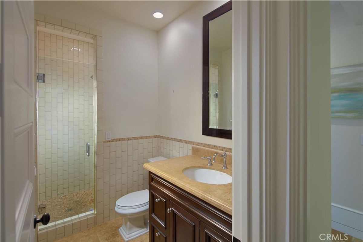 Bathroom with a shower, toilet, and vanity. The walls are tiled.