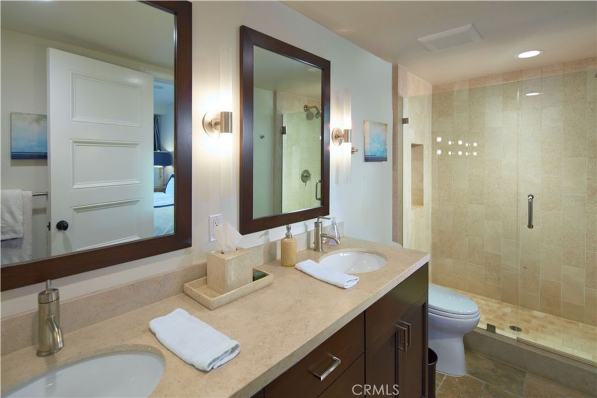 Bathroom with double sinks, a shower, and a toilet. The counters are light-colored, and the cabinets are dark brown.