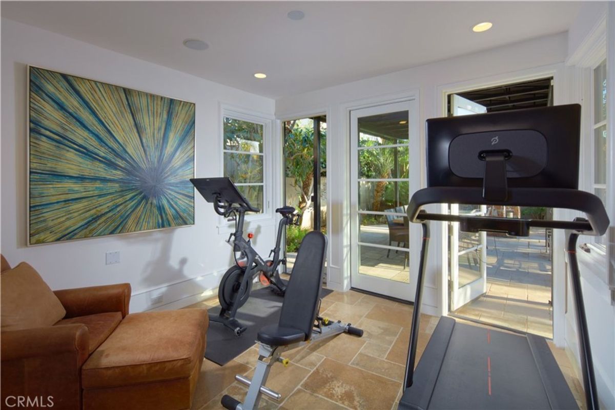 Home gym with a stationary bike, treadmill, and a large piece of abstract art on the wall. There's also a lounge chair and French doors leading to the outside.