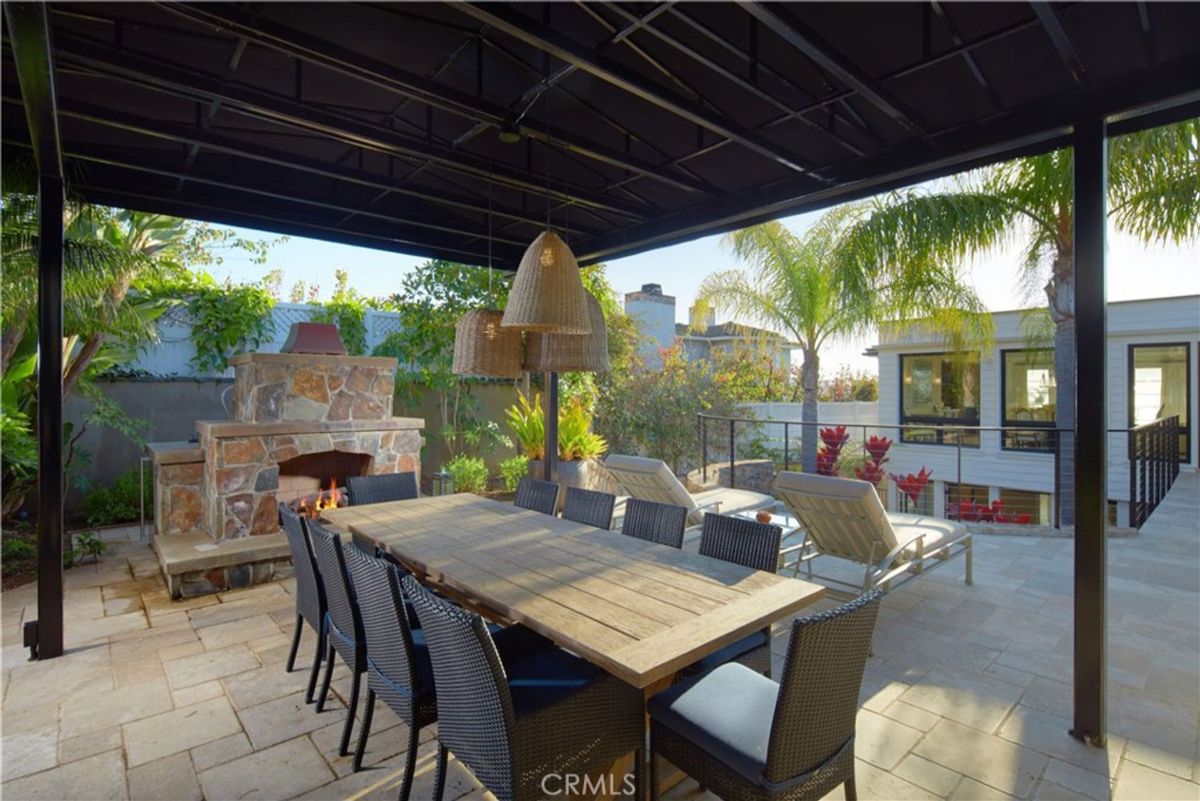 An outdoor dining area features a stone fireplace and shaded seating.