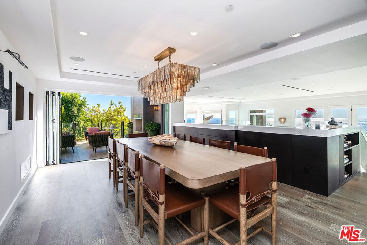 Dining area features long wooden table, leather chairs, and dramatic chandelier; access to outdoor patio is visible.