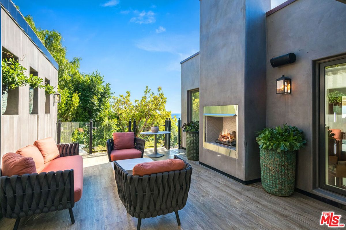 Outdoor patio boasts modern furniture, fireplace, and ocean views.