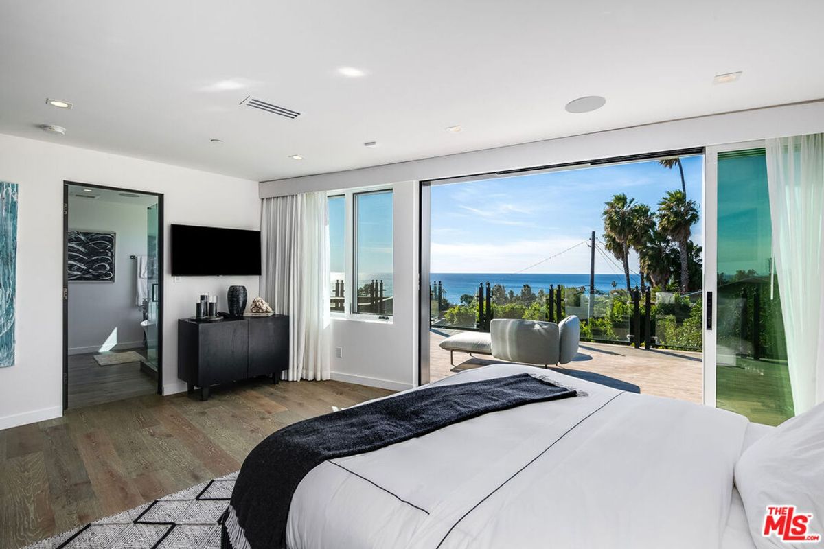 Ocean-view bedroom features floor-to-ceiling windows, a large bed, and access to a private balcony.