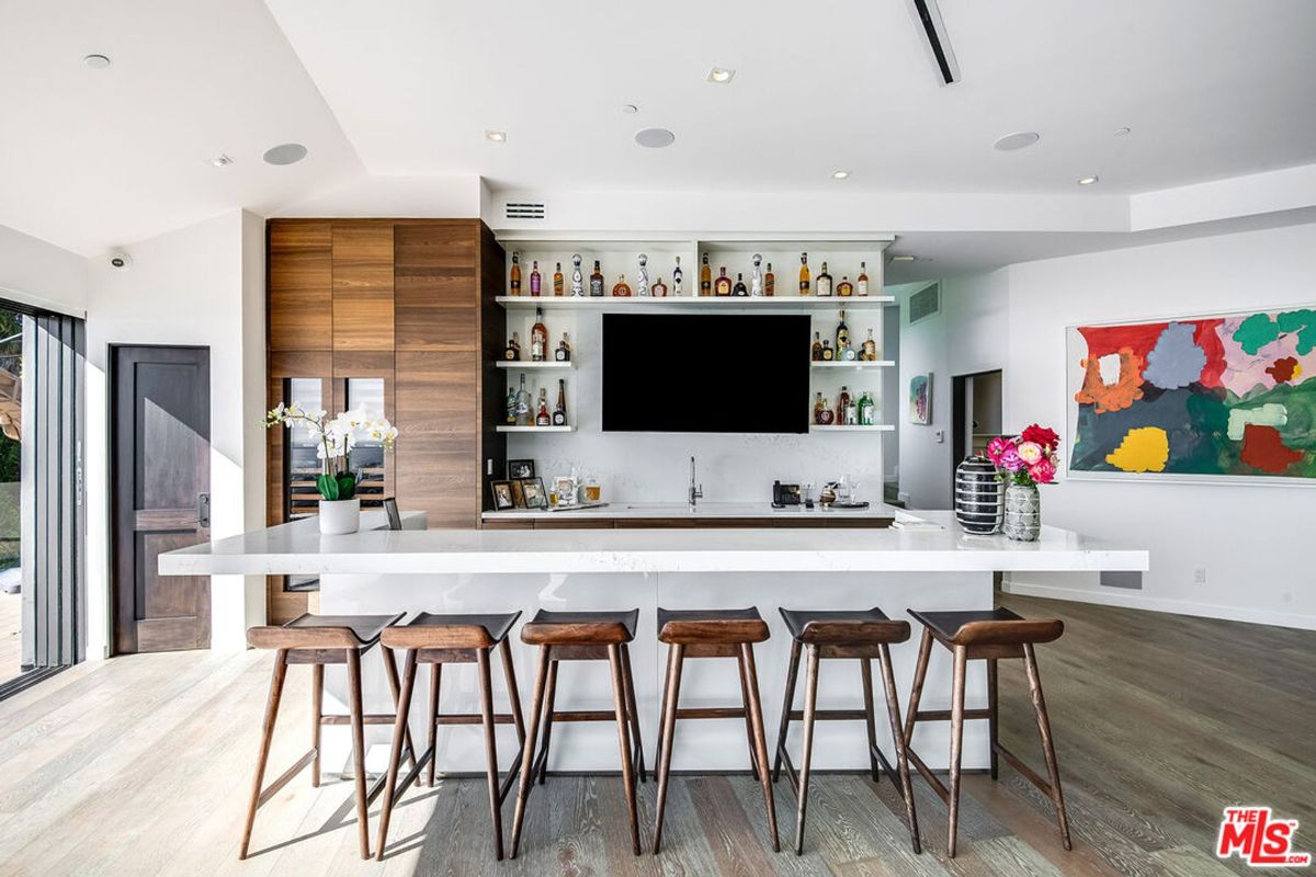 Home bar area features a long island, ample shelving, and modern bar stools.