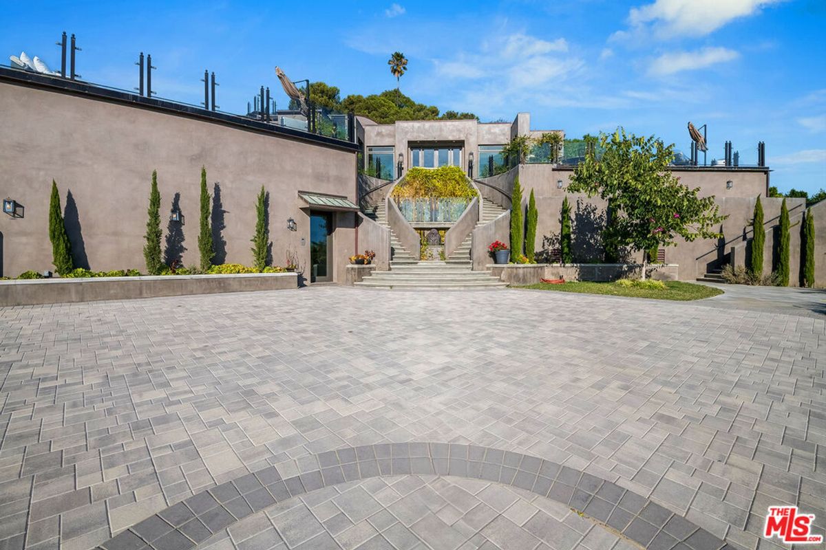 Mediterranean-style mansion, expansive paved courtyard, dual curving staircases, verdant landscaping.