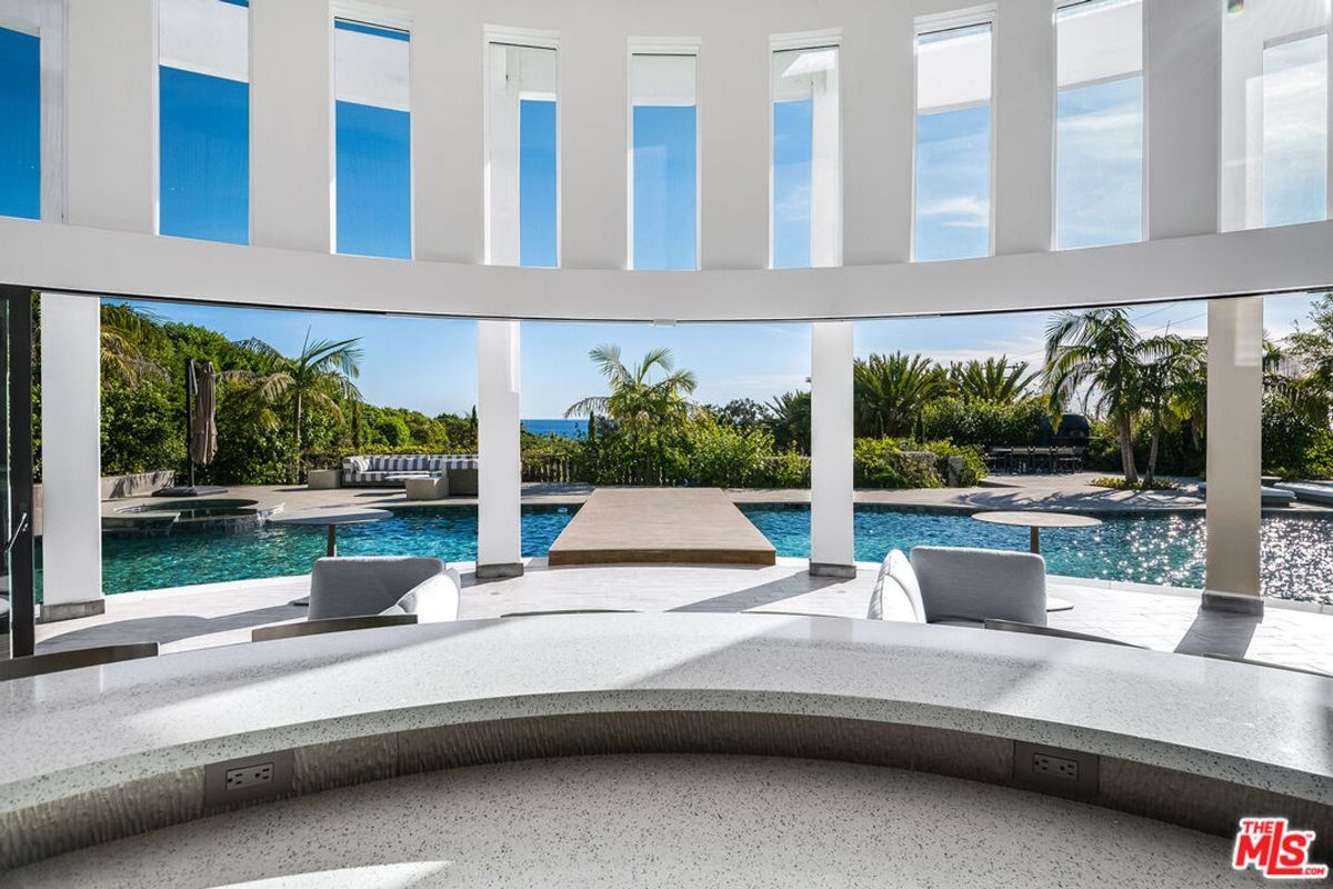 Indoor/outdoor bar area with a curved design and floor-to-ceiling windows offering scenic views of a pool and ocean.