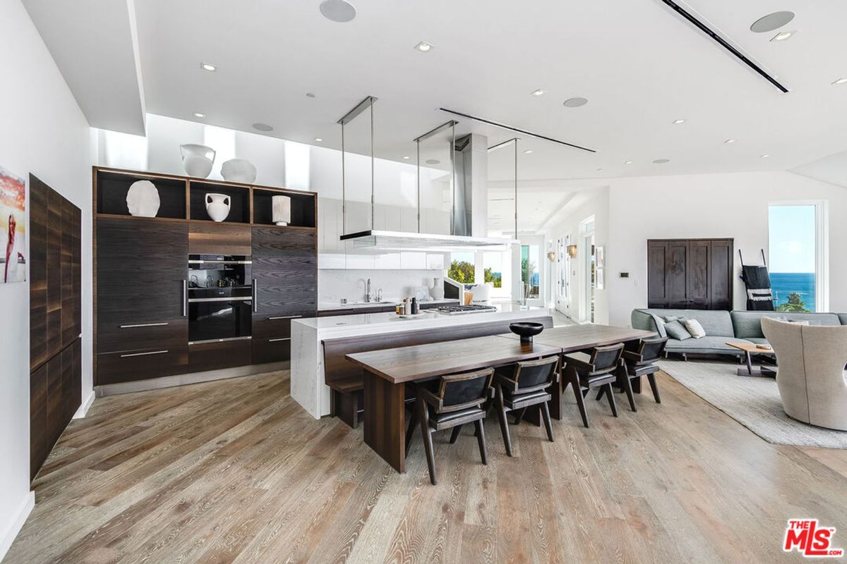 Modern kitchen boasts expansive island, large dining table, and ocean views.